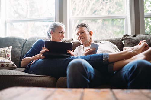 older couple sit on couch looking at tablet and smart phone