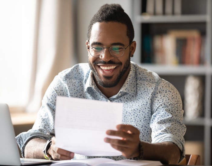 Man with glasses in a home setting is smiling while reading a document