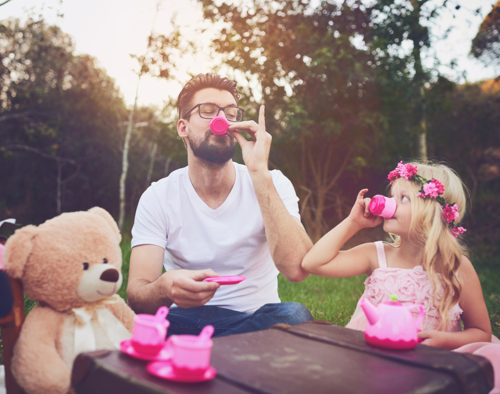 dad and daughter sip tea from a pretend tea set at a child's table