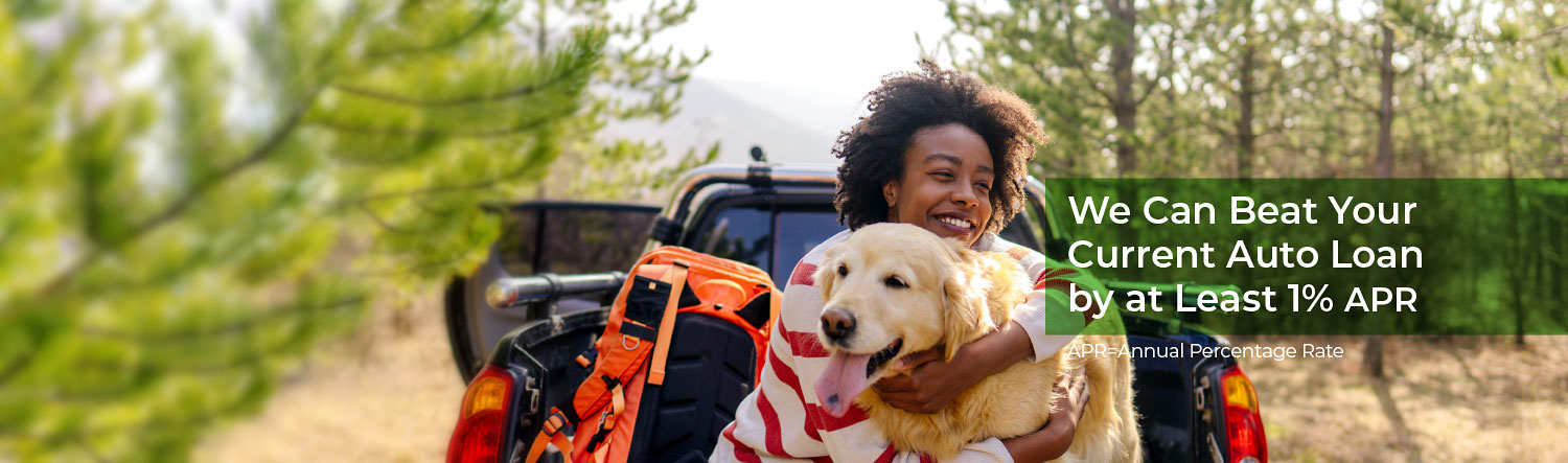 In the woods, a woman sits on the tailgate of her truck smiling while hugging her golden retriever. Text reads we can beat your current auto loan by at least 1% APR. APR= Annual percentage rate.