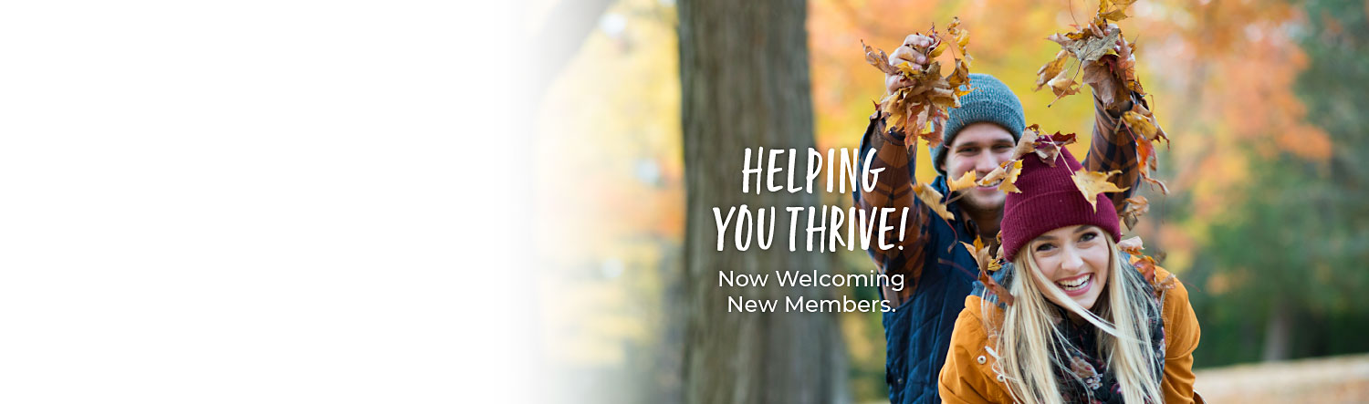 Young couple playing with leaves on a fall day in the woods. Text reads Helping you thrive! Now welcoming new members.