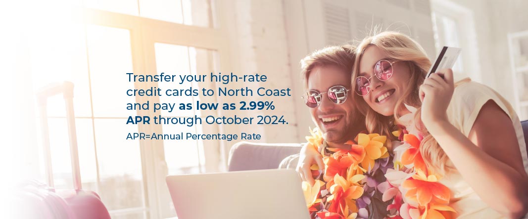 Young couple wearing sunglasses and leis sitting on a couch looking at a laptop on the man’s lap. The woman has her arm around him holding a credit card. Text reads Transfer your high-rate credit cards to north coast and pay as low as 2.99% APR through October 2024. APR=Annual Percentage rate. 