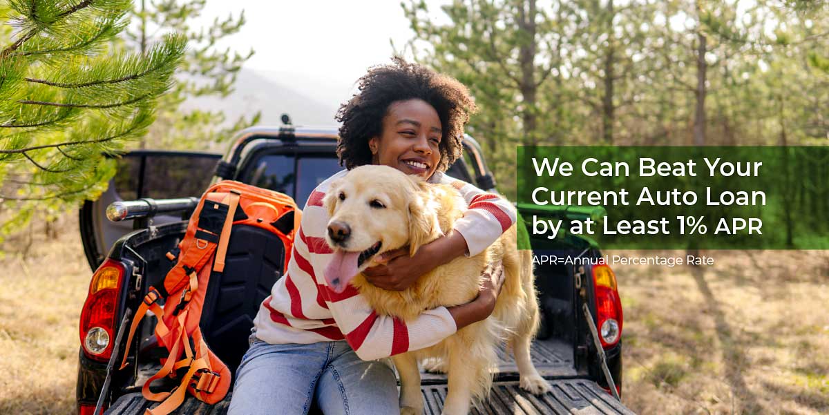 In the woods, a woman sits on the tailgate of her truck smiling while hugging her golden retriever. Text reads we can beat your current auto loan by at least 1% APR. APR= Annual percentage rate. 