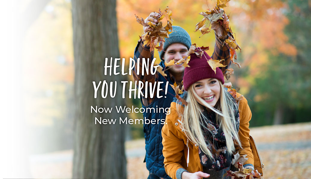 Young couple playing with leaves on a fall day in the woods. Text reads Helping you thrive! Now welcoming new members.