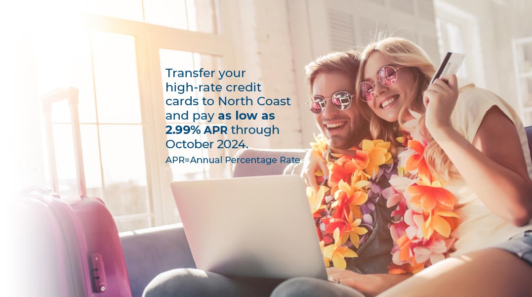 Young couple wearing sunglasses and leis sitting on a couch looking at a laptop on the man’s lap. The woman has her arm around him holding a credit card. Text reads Transfer your high-rate credit cards to north coast and pay as low as 2.99% APR through October 2024. APR=Annual Percentage rate. 