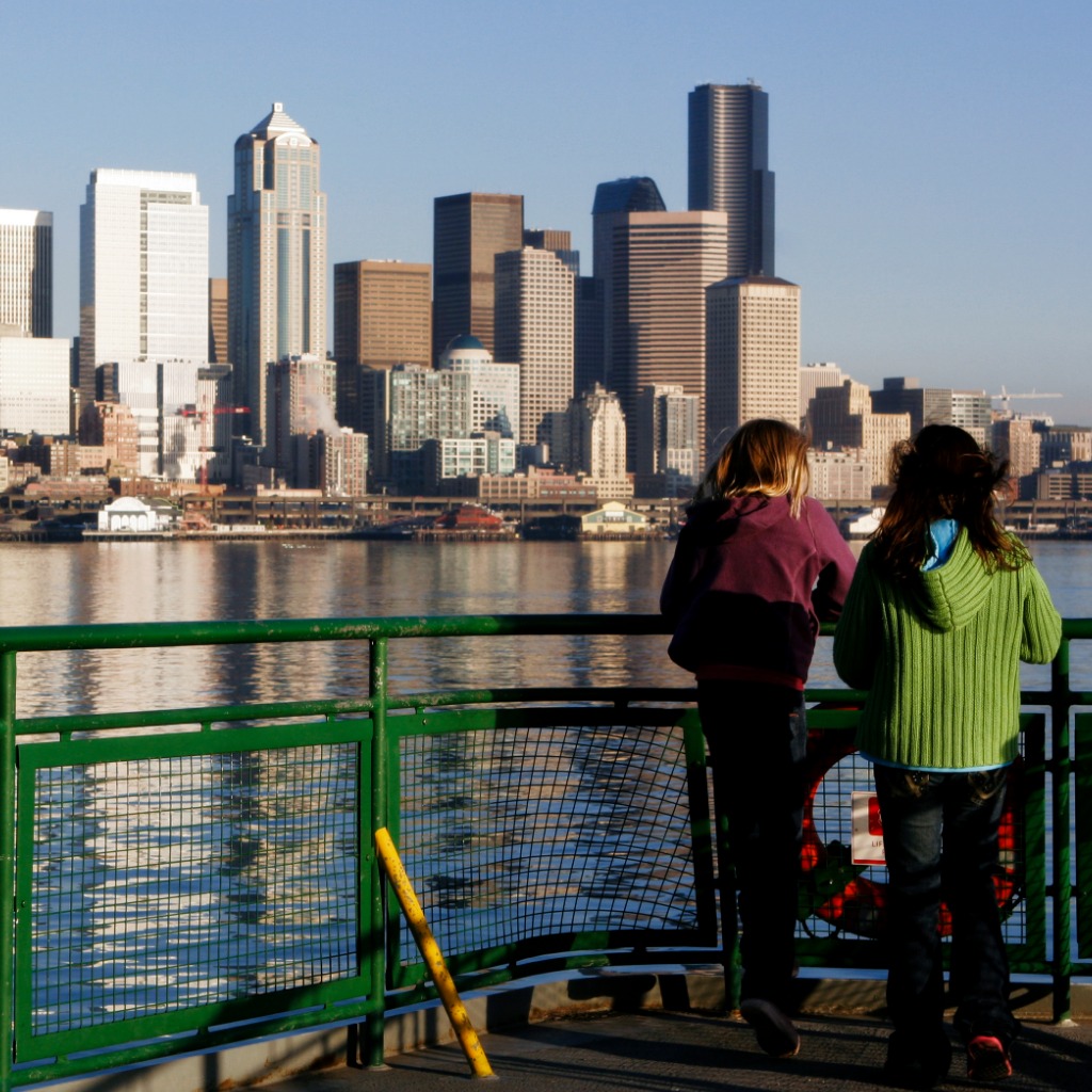 Two people on a ferry with their backs to the camera looking at the Seattle skyline 
