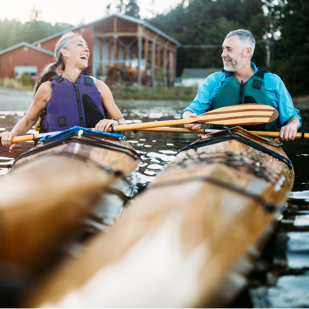Middle aged man and woman in wooden kayaks smiling at eachother