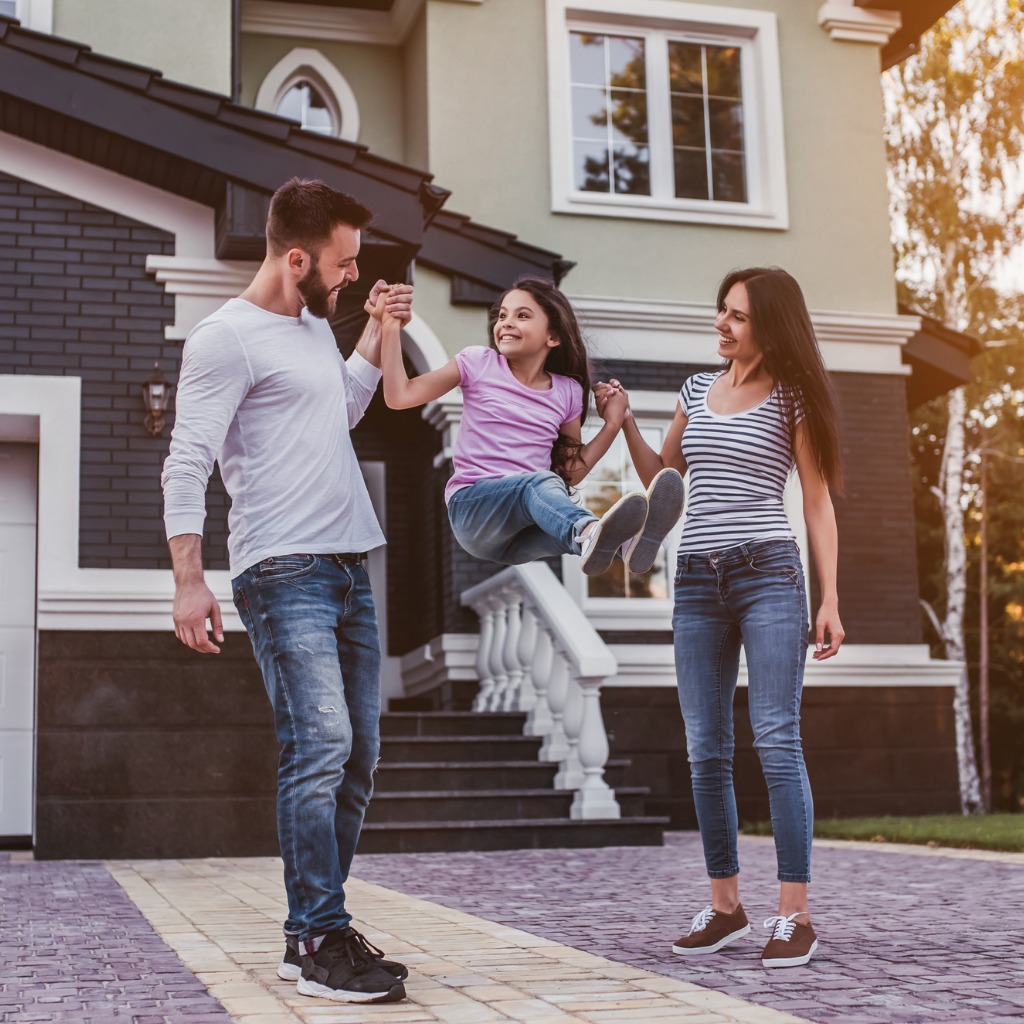 A young couple swings their daughter between them in front of their home