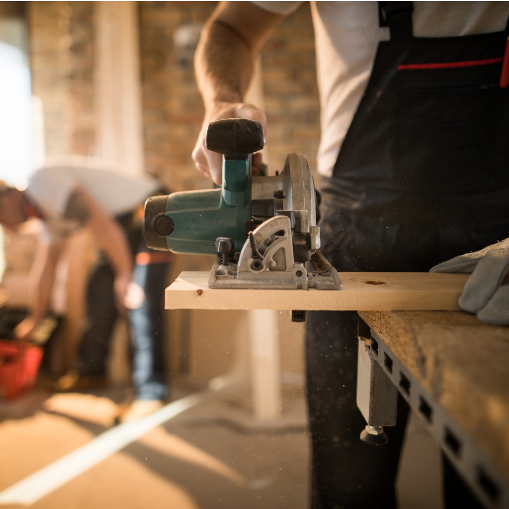 unrecognizable-worker-cutting-plank-with-circular-saw-at-construction-site