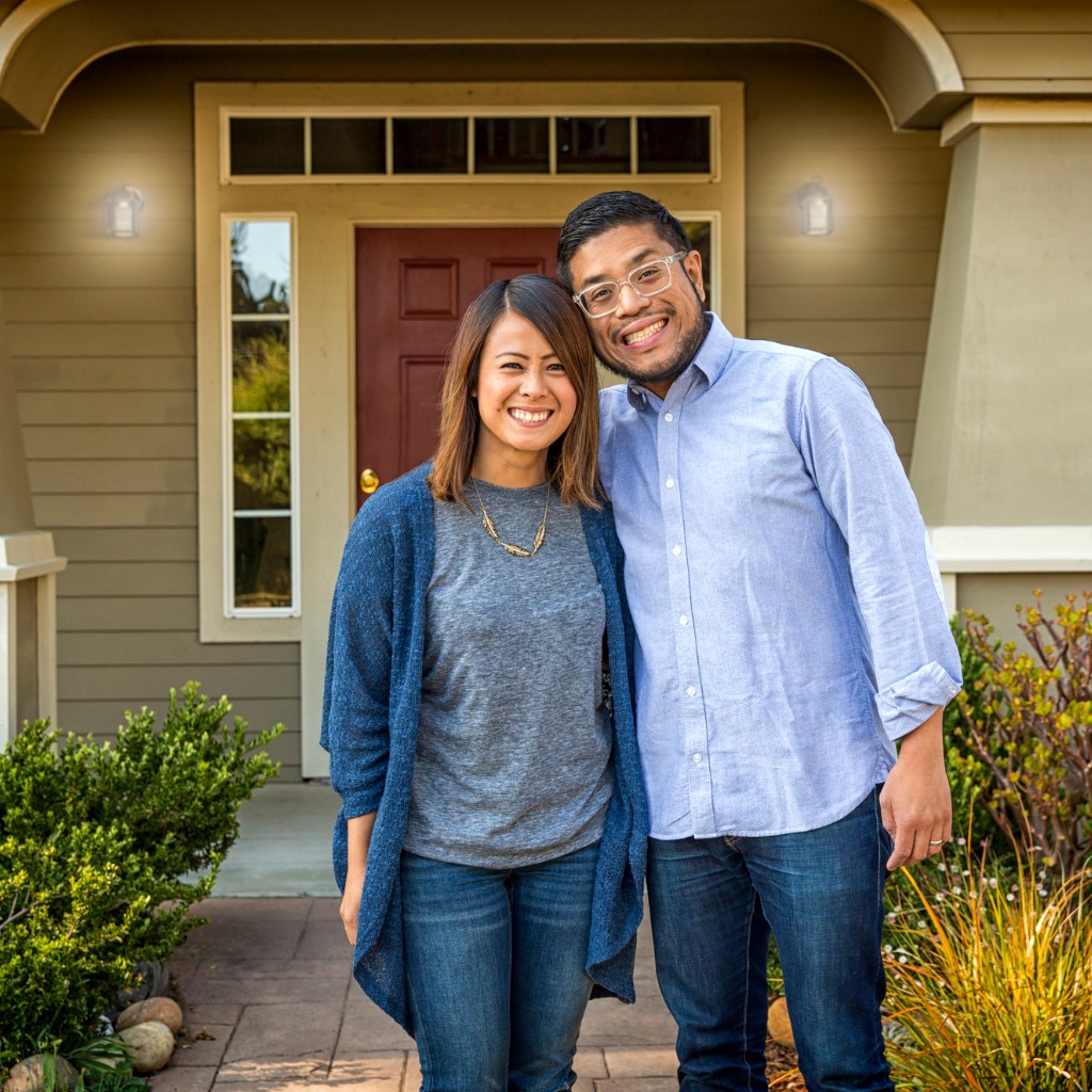 Happy Asian-American couple smiles at the camera in front of their home